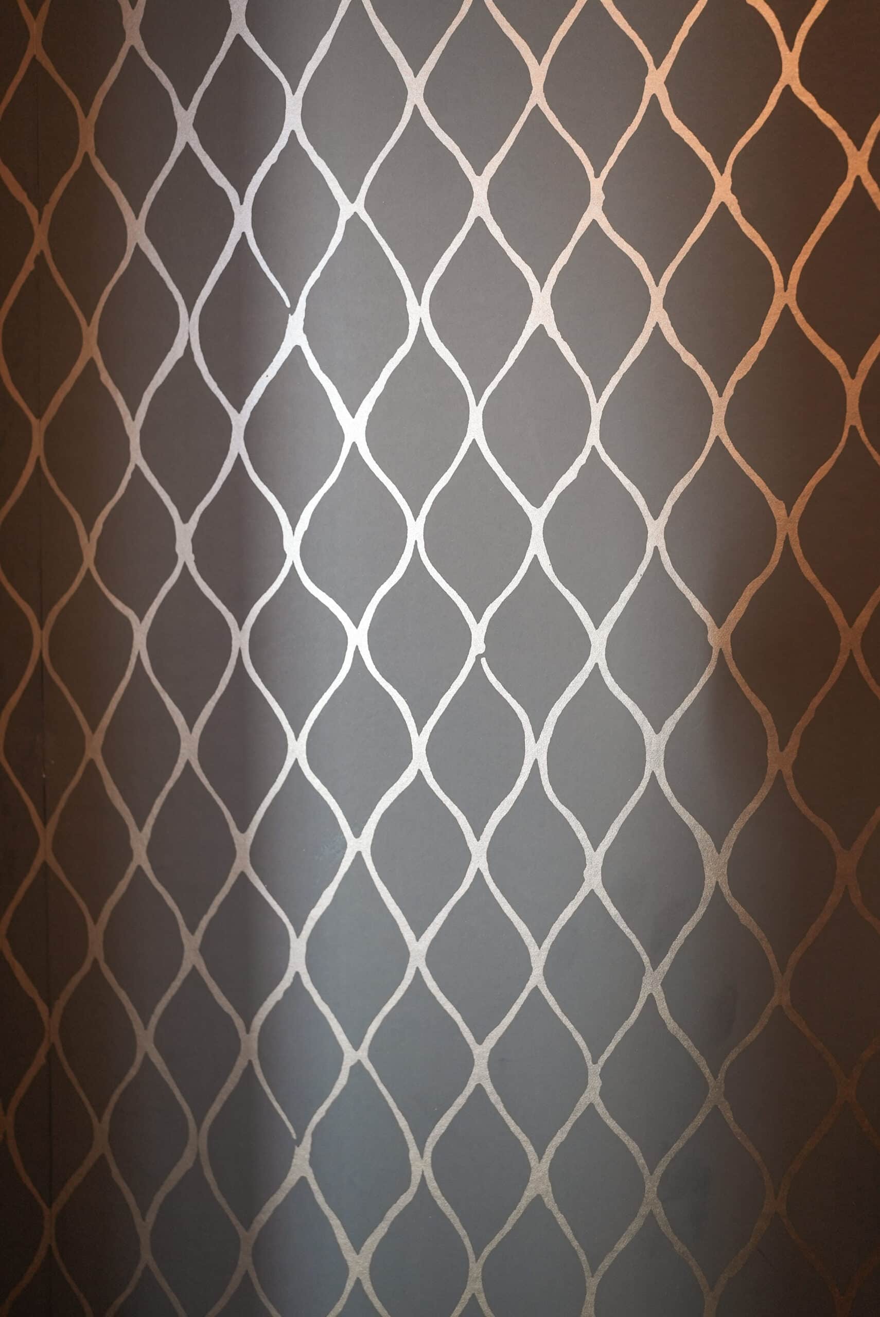 Gray wallpaper with metallic rose-gold trellis lattice pattern.