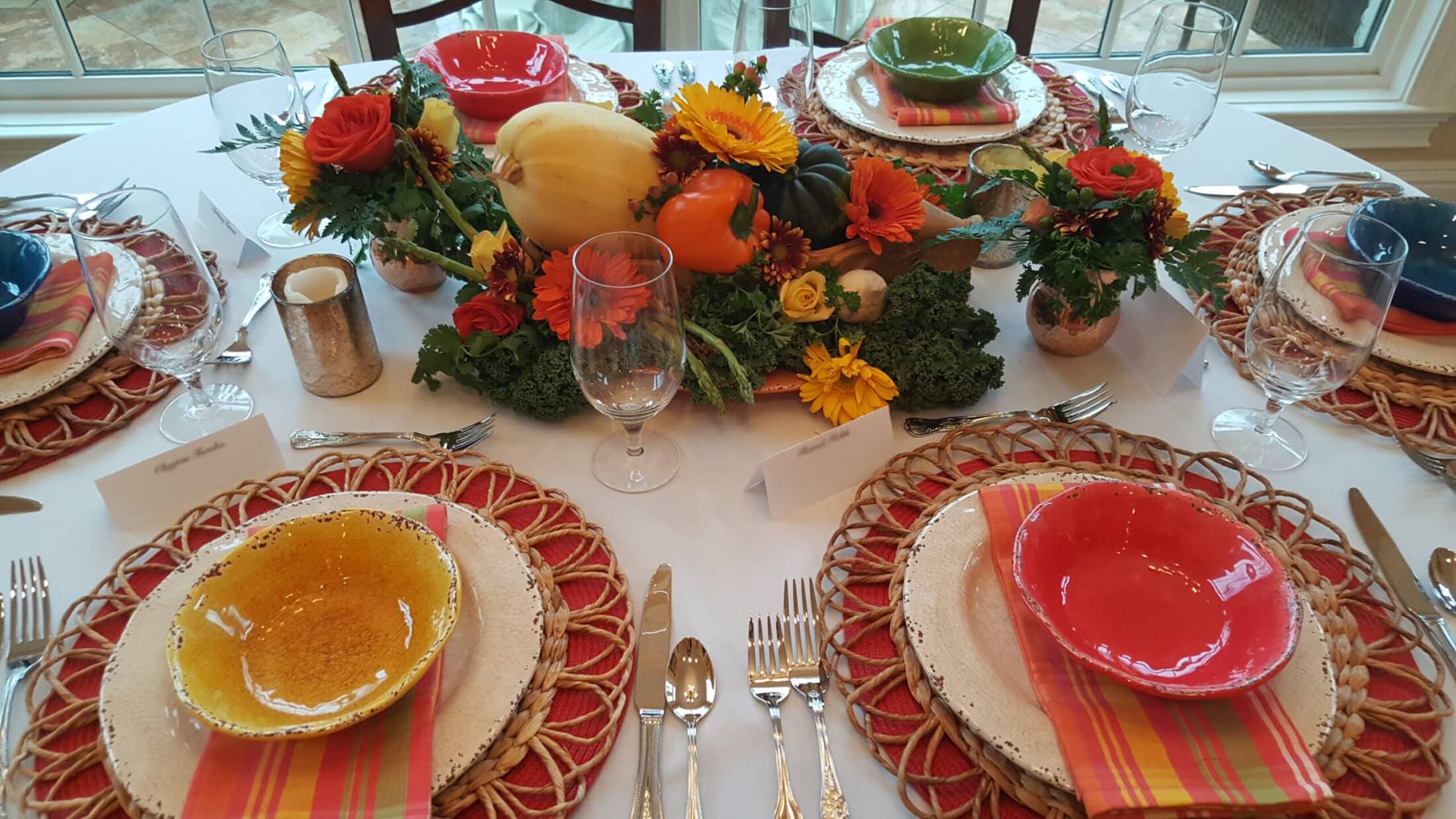 Fall tablescape with colorful place settings, pumpkins and seasonal floral centerpiece